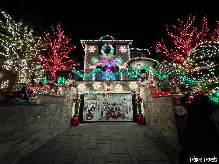 white stone driveway surrounded by matching retainer walls ending with the garage that has Merry Christmas and decorations and red, green, white lights all in the trees on both sides