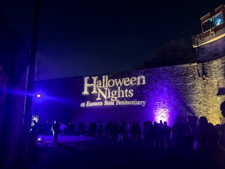 projection of "halloween nights at eastern state penitentiary" lit up against a stone wall against a night sky in philadelphia