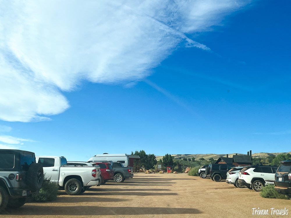 view of the parking lot at the wire pass trailhead with cars on each side against a blue sky in utah
