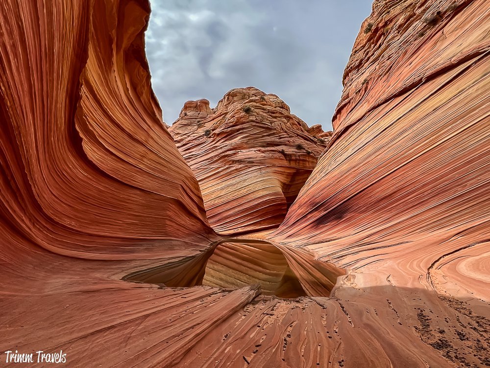 red, orange, yellow swirly sandstone rock against dark gray sky with pudding of water in center
