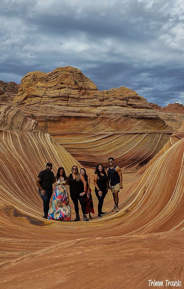 our group of 6 posing on the swirly sandstone formation of the wave against a cloudy dark gray sky in arizona