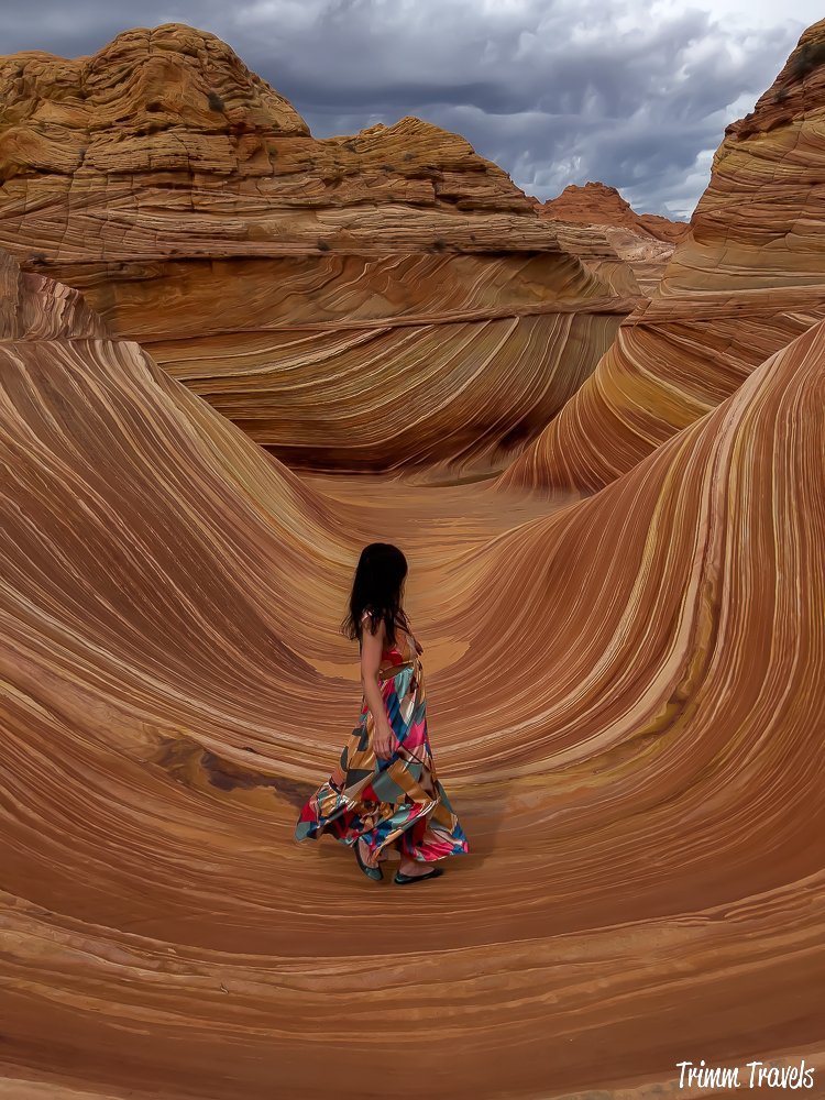 heather from trimm travels posing on the swirly sandstone formations of the wave against a dark gray sky in arizona