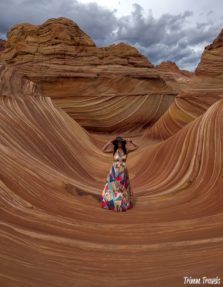 heather from trimm travels posing in a dress on the swirly sandstone formations of the wave against a dark gray sky in arizona