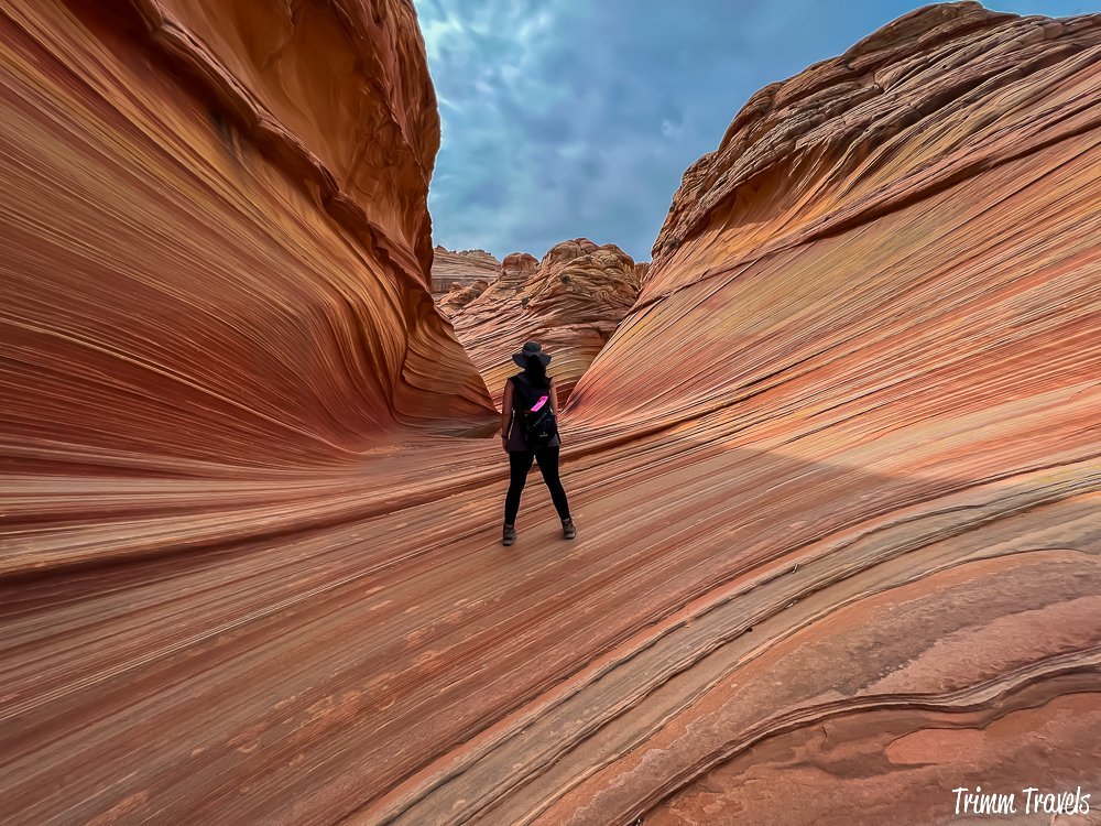 heather from trimm travels standing with back to the camera as she looks in awe at the orange swirly sandstone formation of the wave in arizona