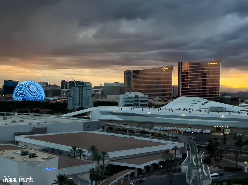 hotel room view out over las vegas nevada with the wynn and encore hotels to the right and the sphere lit up bright blue to the left against an angry sunset sky