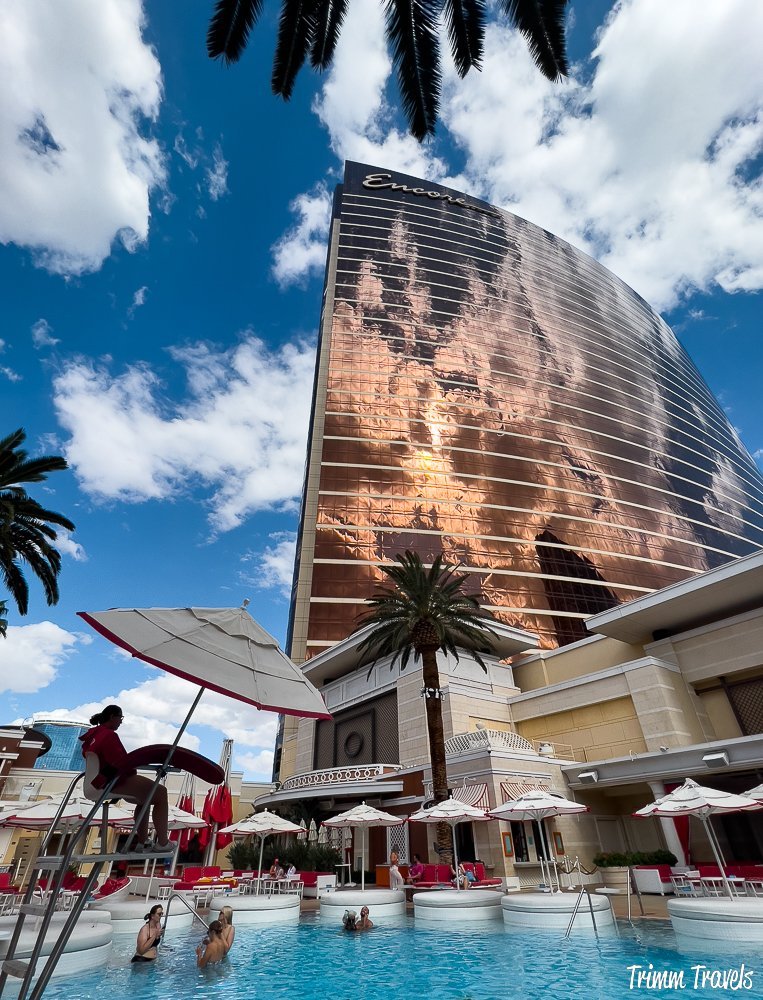 daytime shot of a pool in the foreground looking straight up at the encore against a blue sky and framed with palm trees in las vegas nevada