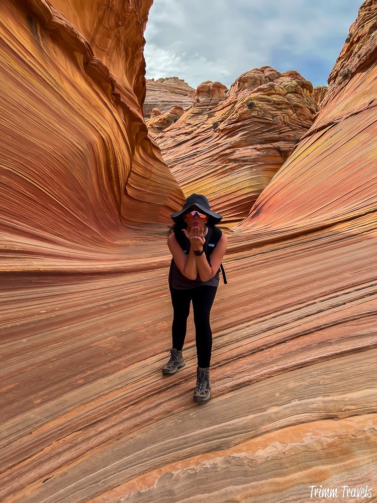 heather from trimm travels blowing a kiss while standing on the swirly sandstone formation of the wave in arizona
