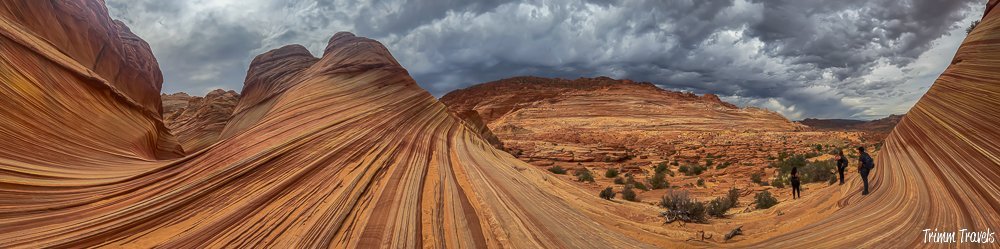 panorama of the orange swirly sandstone formations of the wave in arizona against a very dark, cloudy gray sky