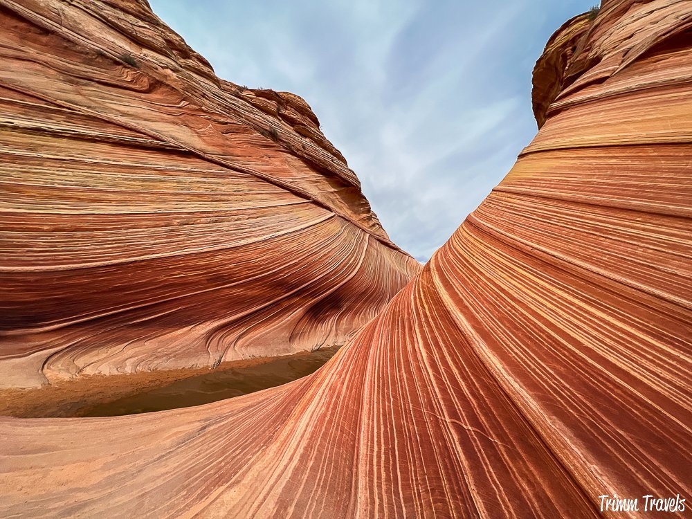 swirly sandstone formations of the wave coming together with blue sky in the middle and water peeking out to the bottom left