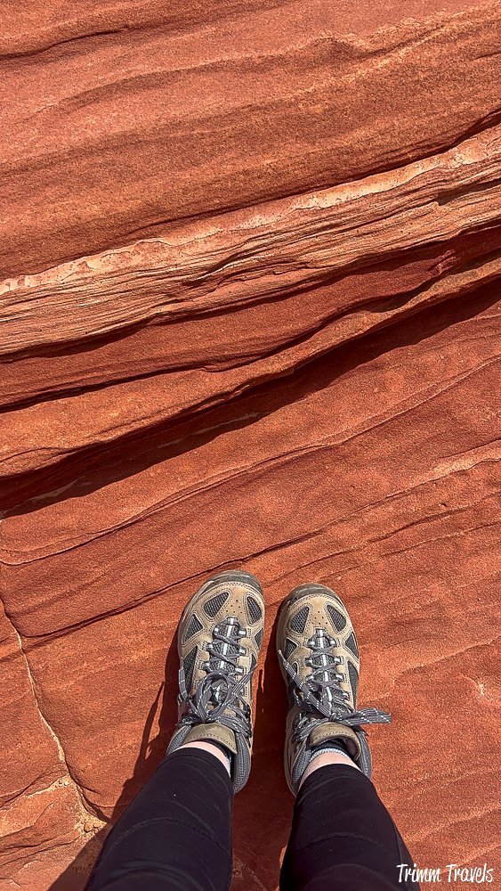 heather from trimm travels looking straight down at her boots and the striking orange sandstone of the wave in arizona