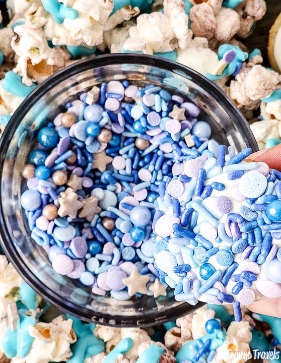 close up shot of a mini cupcake dipped in blue and purple sprinkles and surrounded by popcorn