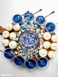 fully assembled mermaid charcuterie board with blue jello cups, mini white cupcakes, decorated popcorn, and blue and purple sprinkles on a white background