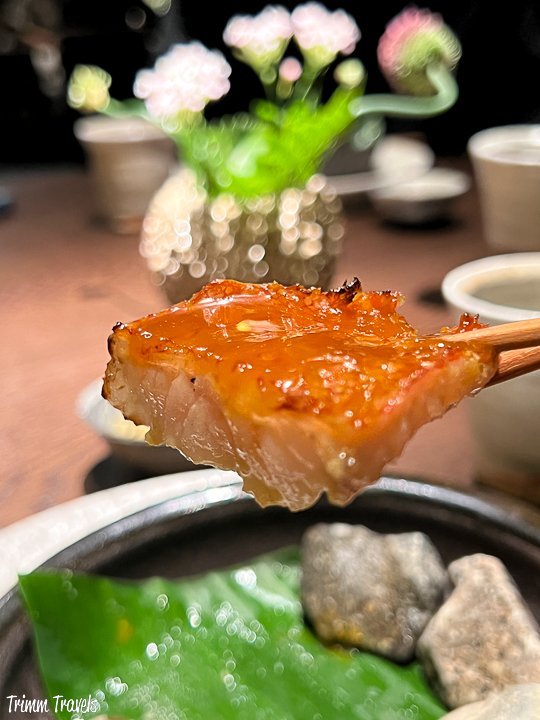 closeup of a square piece of orange fish on chopsticks