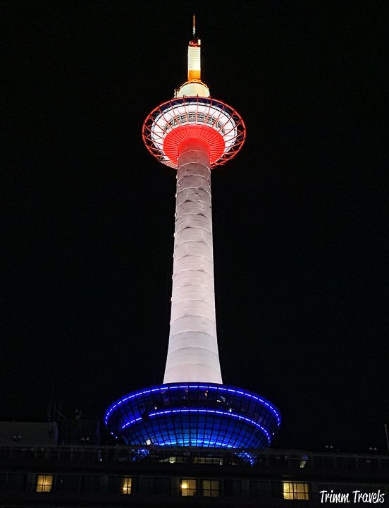 looking straight up at kyoto tower at night with its white, orange, and blue colors