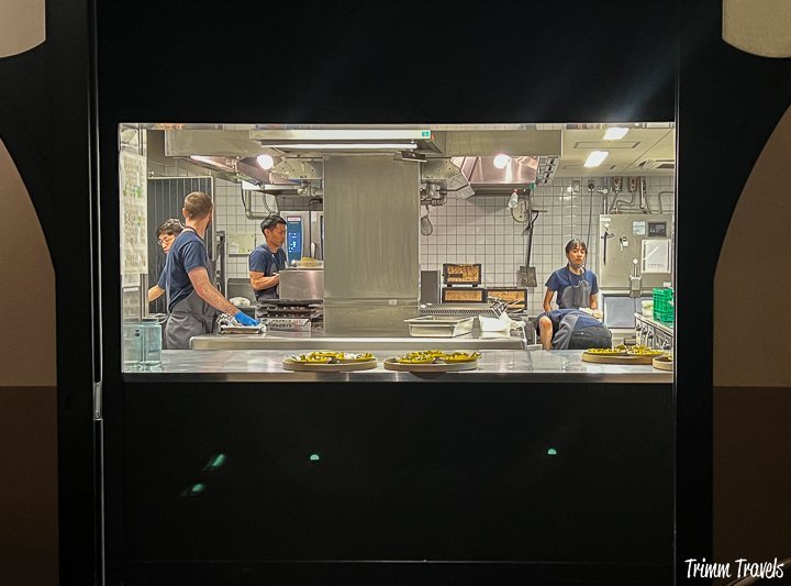 peak through to the working kitchen of noma with 5 employees wearing navy shirts