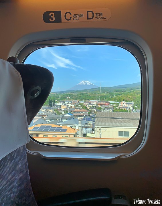 mount fuji in the horizon outside a small window of a japanese bullet train