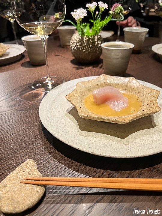 piece of fish on yellow sauce with chopsticks in the foreground